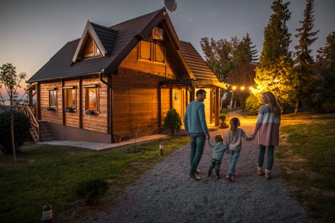 Rear view of happy family holding hands and walking by their chalet in the evening.