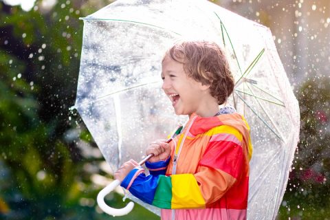 Child playing in autumn rain. Kid with umbrella.
